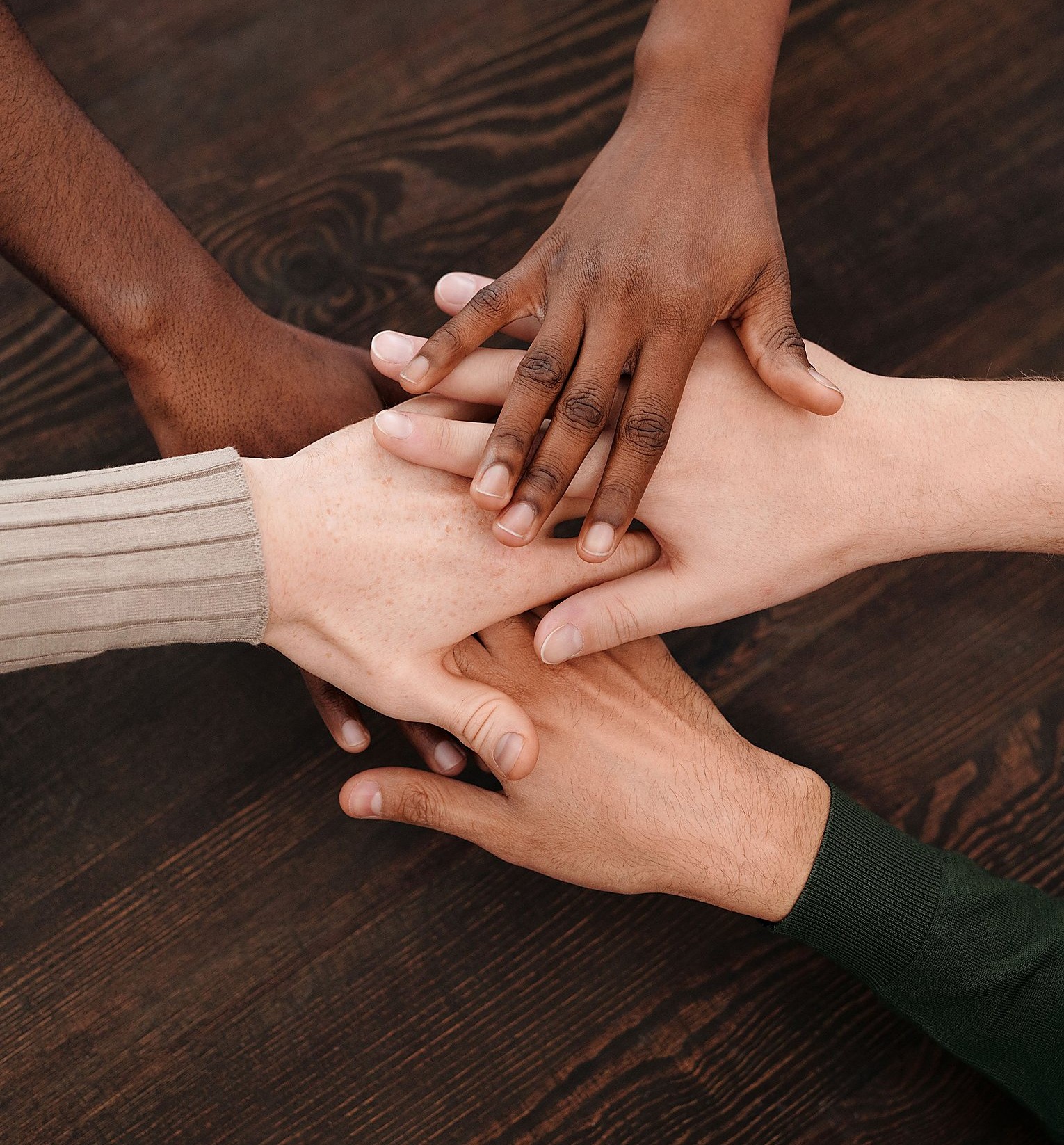 A diverse group of hands stacked together on a wooden table